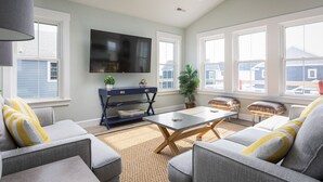 A spacious living room with a flat-screen TV mounted on the wall, a dark blue console table with decorative items, a coffee table, and a large window offering a view of the outside. - Dog Friendly - Sound View Home on private harbor. Amazing Sunsets-Fishing-Dock (Salvo)