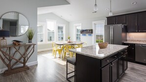 A modern kitchen with dark cabinetry, a granite countertop, and a dining area with yellow chairs. - Dog Friendly - Sound View Home on private harbor. Amazing Sunsets-Fishing-Dock (Salvo)