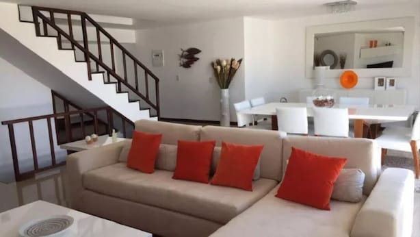 Una sala de estar moderna con un sofá seccional color beige, una mesa de centro blanca y una escalera que conduce a un piso superior.