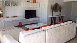 Una sala de estar moderna con un sofá blanco, un televisor de pantalla plana montado en la pared y una mesita con adornos.