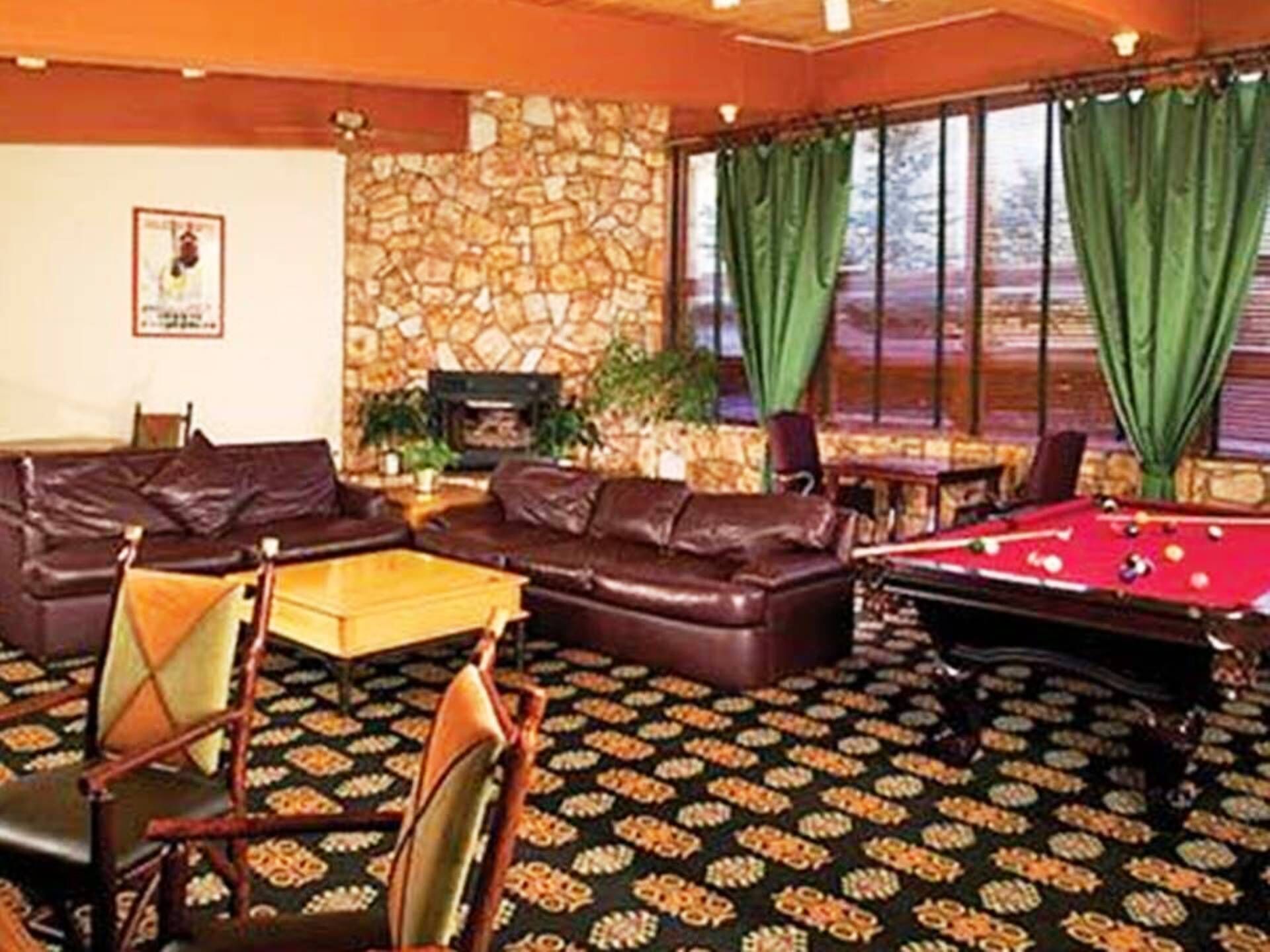 Una habitación con mesa de billar, sofás de cuero, alfombra estampada, pared de piedra y chimenea.