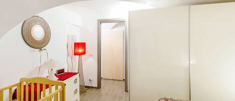 A bedroom with a crib, a wardrobe, a bedside table with a lamp, and a patterned bedspread.