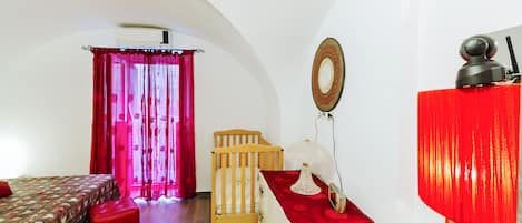 A bedroom with a bed, a crib, a red lamp, and a mirror on the wall.