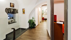 Un pasillo con piso de madera, barandilla de cristal, pared de piedra y una planta.