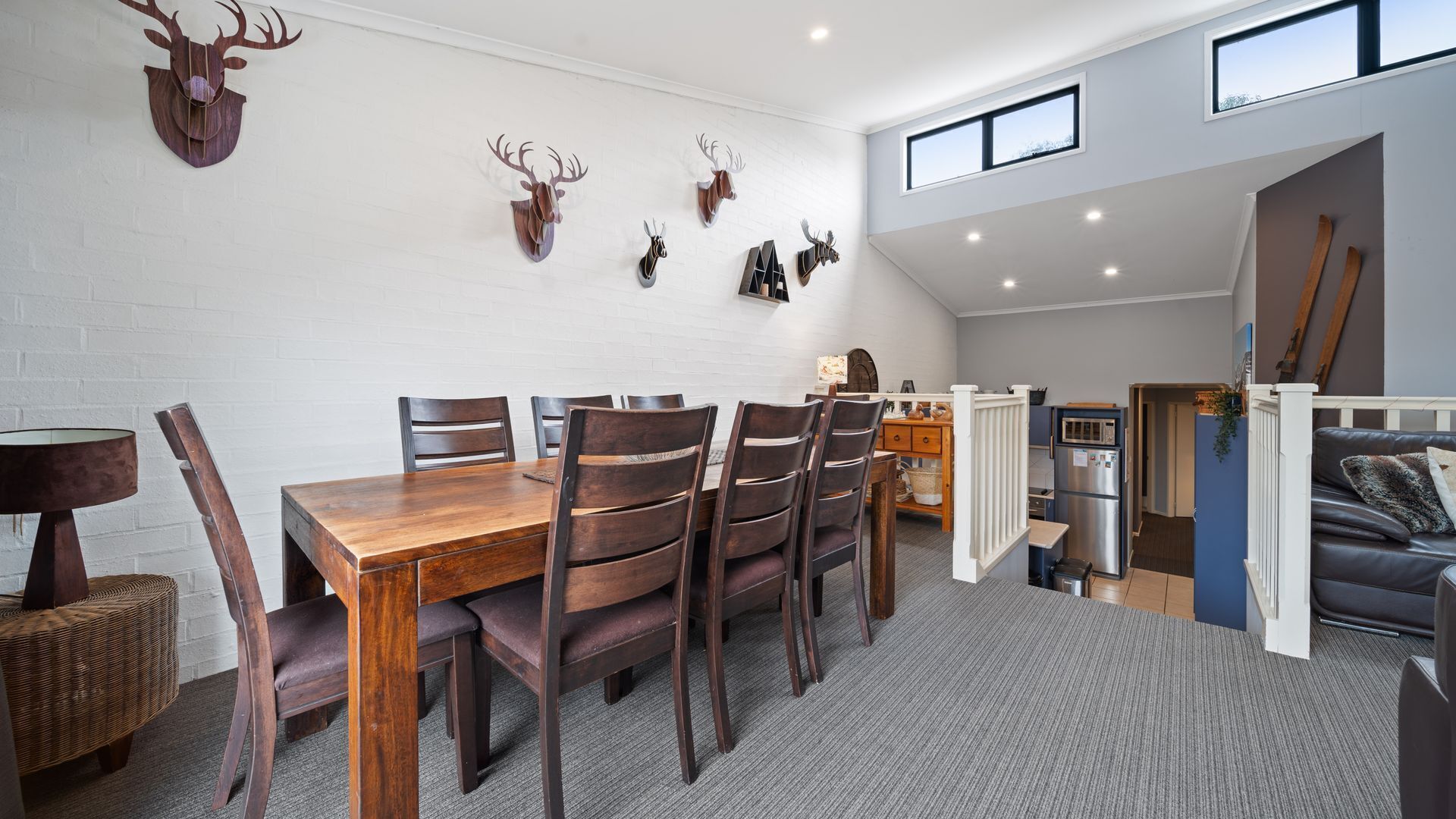 Un coin repas avec une table et des chaises en bois, une cuisine équipée d’un réfrigérateur et un espace en mezzanine avec une fenêtre.