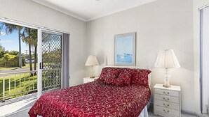 Un dormitorio con una cama grande, dos mesitas de noche, una ventana con vistas a la vegetación y un cuadro en la pared.