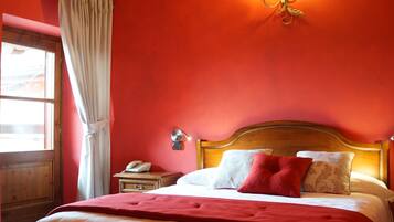 A bedroom with a wooden bed, red walls, a wooden ceiling, a bedside table with a lamp, and a window with curtains.
