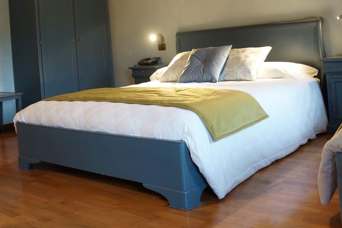 A bedroom with a bed, wooden beams, a wardrobe, and a nightstand with a lamp.