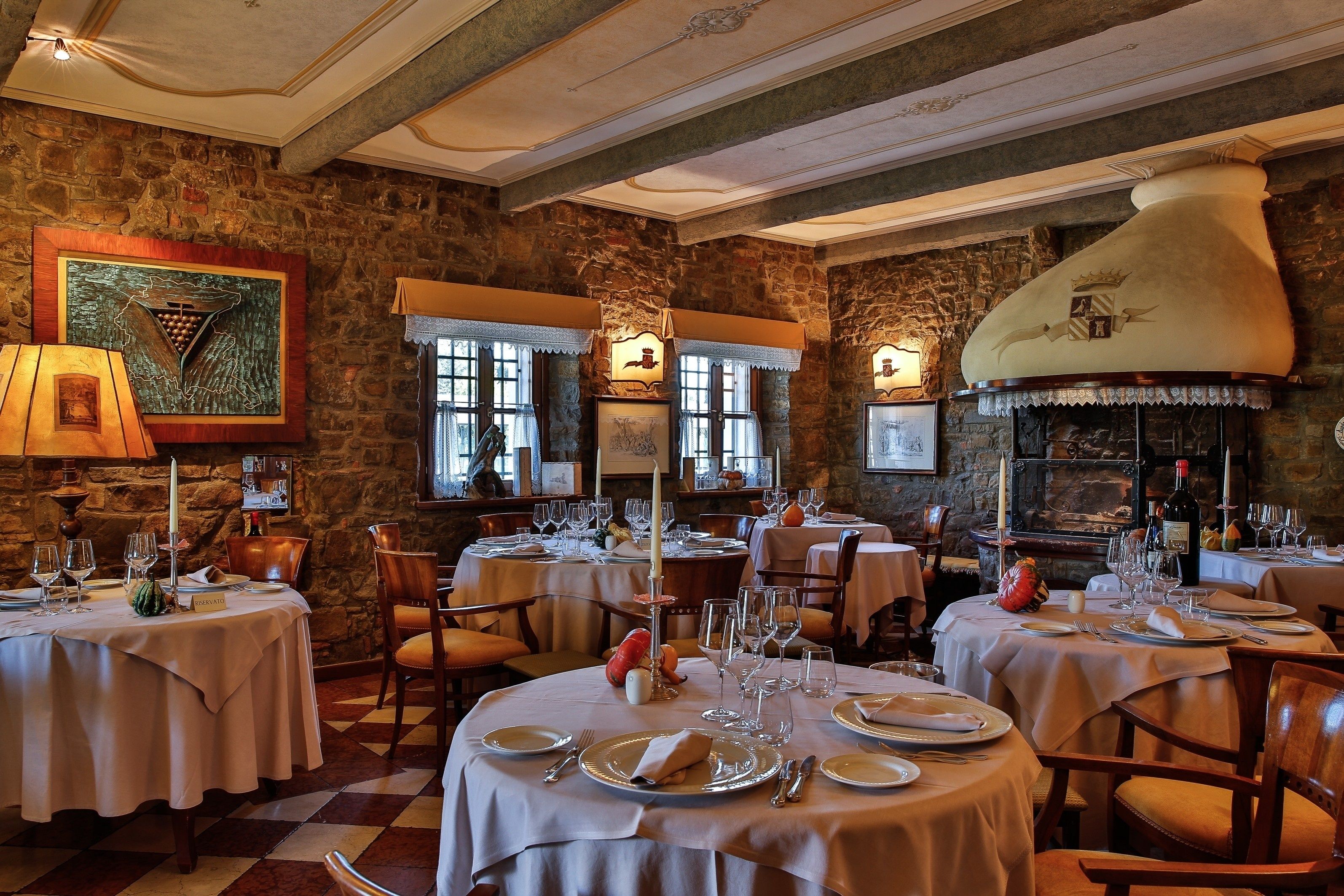 A restaurant with stone walls, round tables set with white tablecloths, and a large chimney.