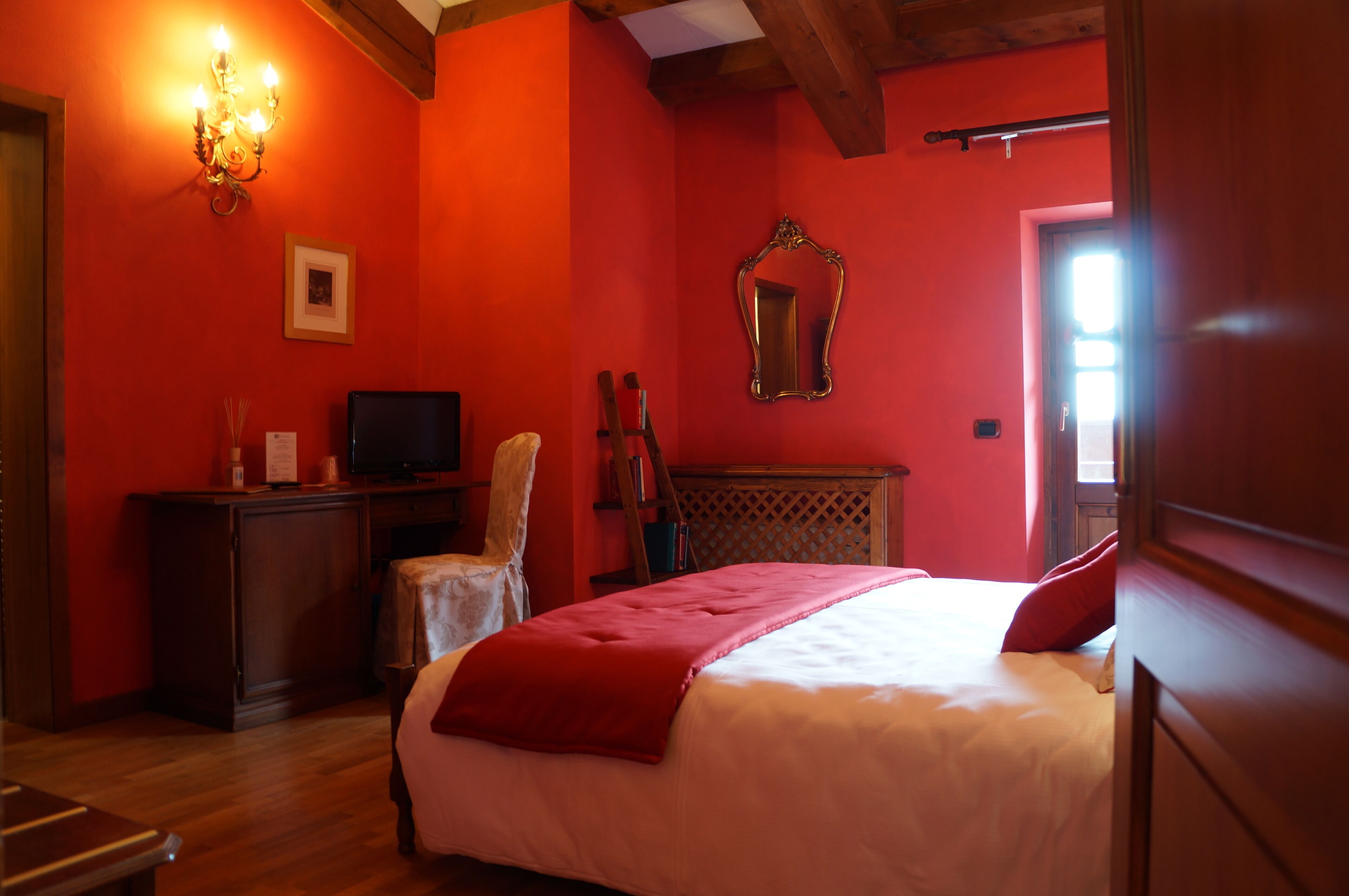 A bedroom with a red wall, a wooden bed, a television, a chair, and a mirror.