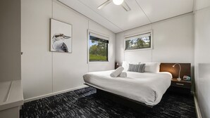 Ein modernes Hotelzimmer mit einem großen Bett, zwei Fenstern, einem Nachttisch und einer Wandlampe.