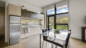 Eine moderne Küche mit Edelstahlgeräten, einem Glastisch und Blick auf einen Wald durch große Fenster.