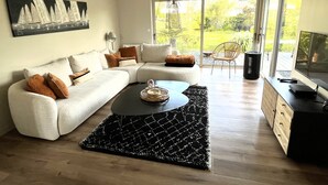 A modern living room with a sectional sofa, a coffee table, and a large window offering a view of greenery. - House 200m from the sea in BENODET - 4 bedrooms: all on foot! (Bénodet)