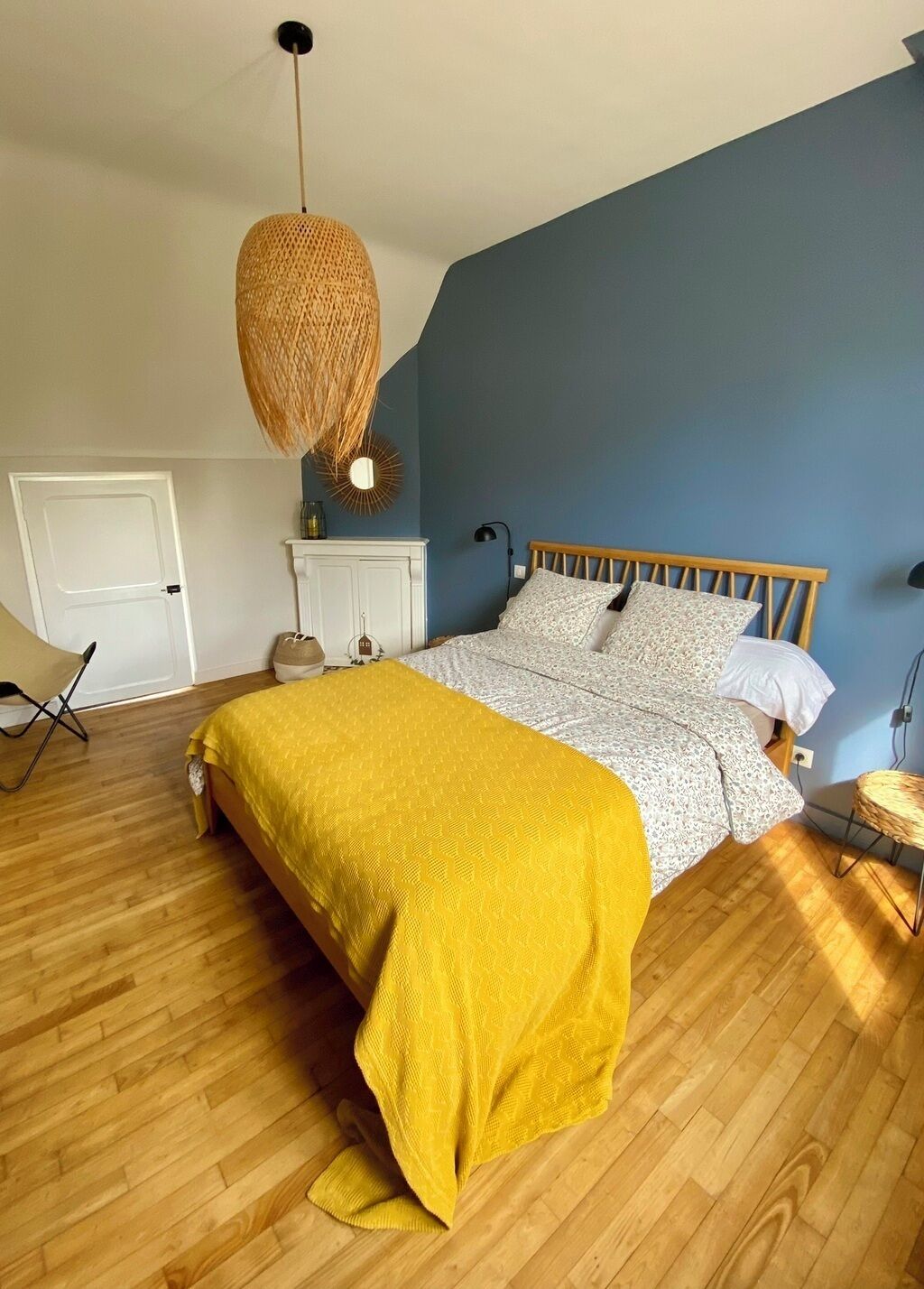 Een slaapkamer met een bed, een gele plaid, een hanglamp en een witte deur.
