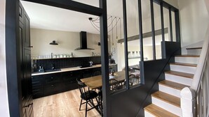 A modern kitchen with dark cabinetry, a wooden dining table, and a staircase with white railings. - House 200m from the sea in BENODET - 4 bedrooms: all on foot! (Bénodet)