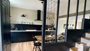 A modern kitchen with dark cabinetry, a wooden dining table, and a staircase with wooden steps. - House 200m from the sea in BENODET - 4 bedrooms: all on foot! (Bénodet)