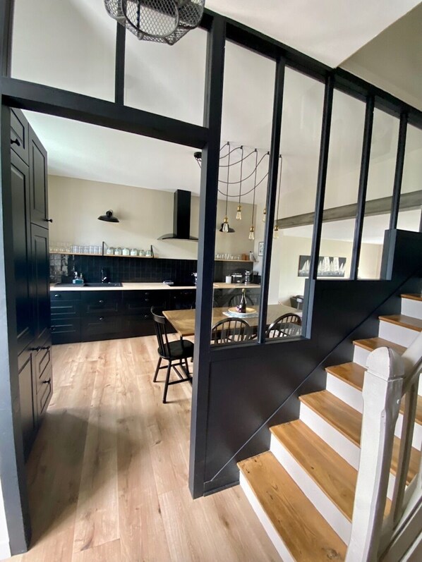 A modern kitchen with dark cabinetry, a wooden dining table, and a staircase with wooden steps.