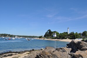 A coastal scene with a lighthouse, rocky shoreline, and boats in the water.