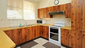 Una cocina pequeña con armarios de madera, microondas, estufa y ventana con persianas.