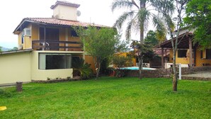 Uma casa de dois andares com telhado de telhas, piscina e gramado bem cuidado.
