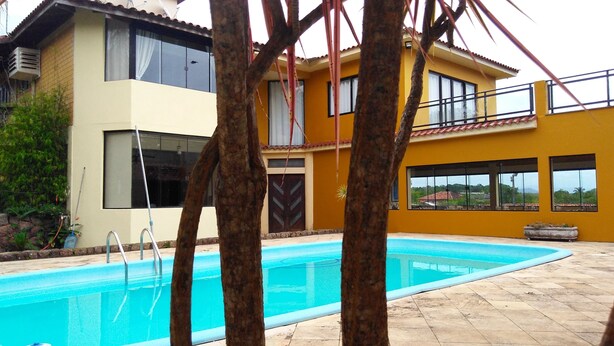 Uma casa de dois andares com piscina, janelas amplas e varanda.