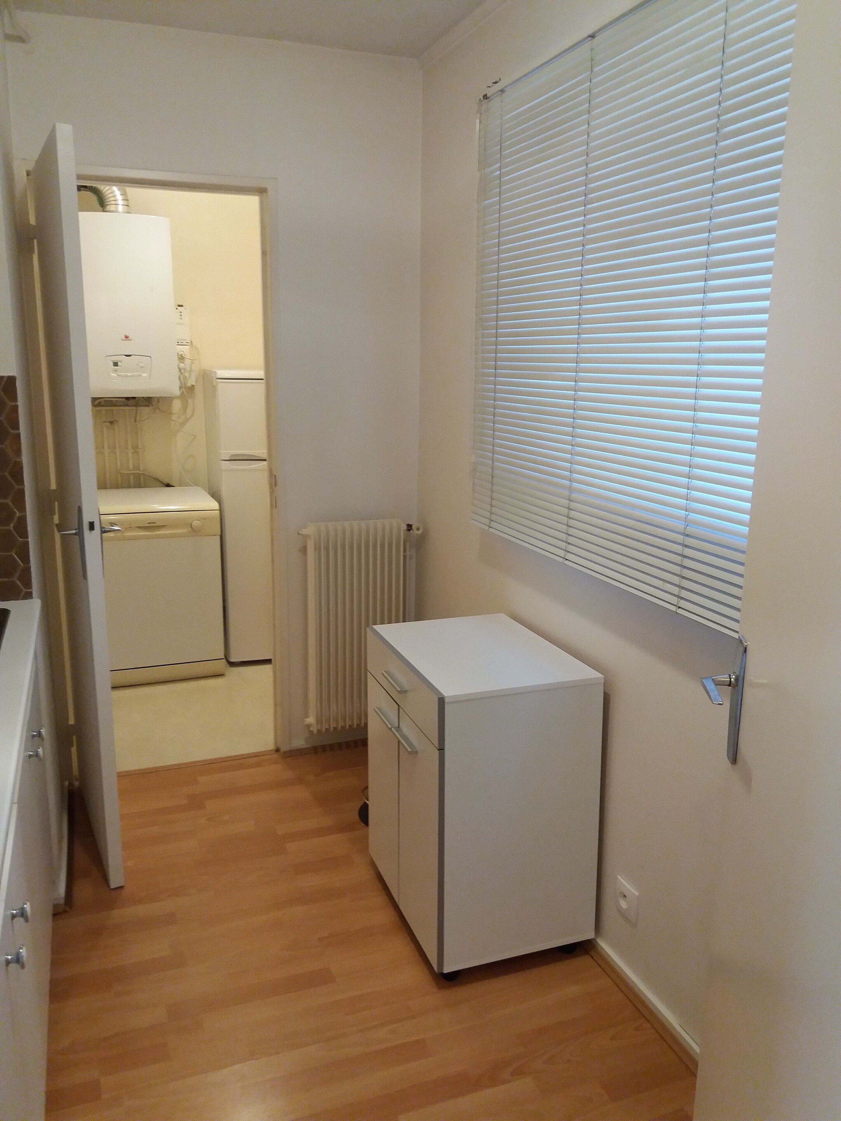 A compact kitchen with a refrigerator, a built-in oven, and a radiator.