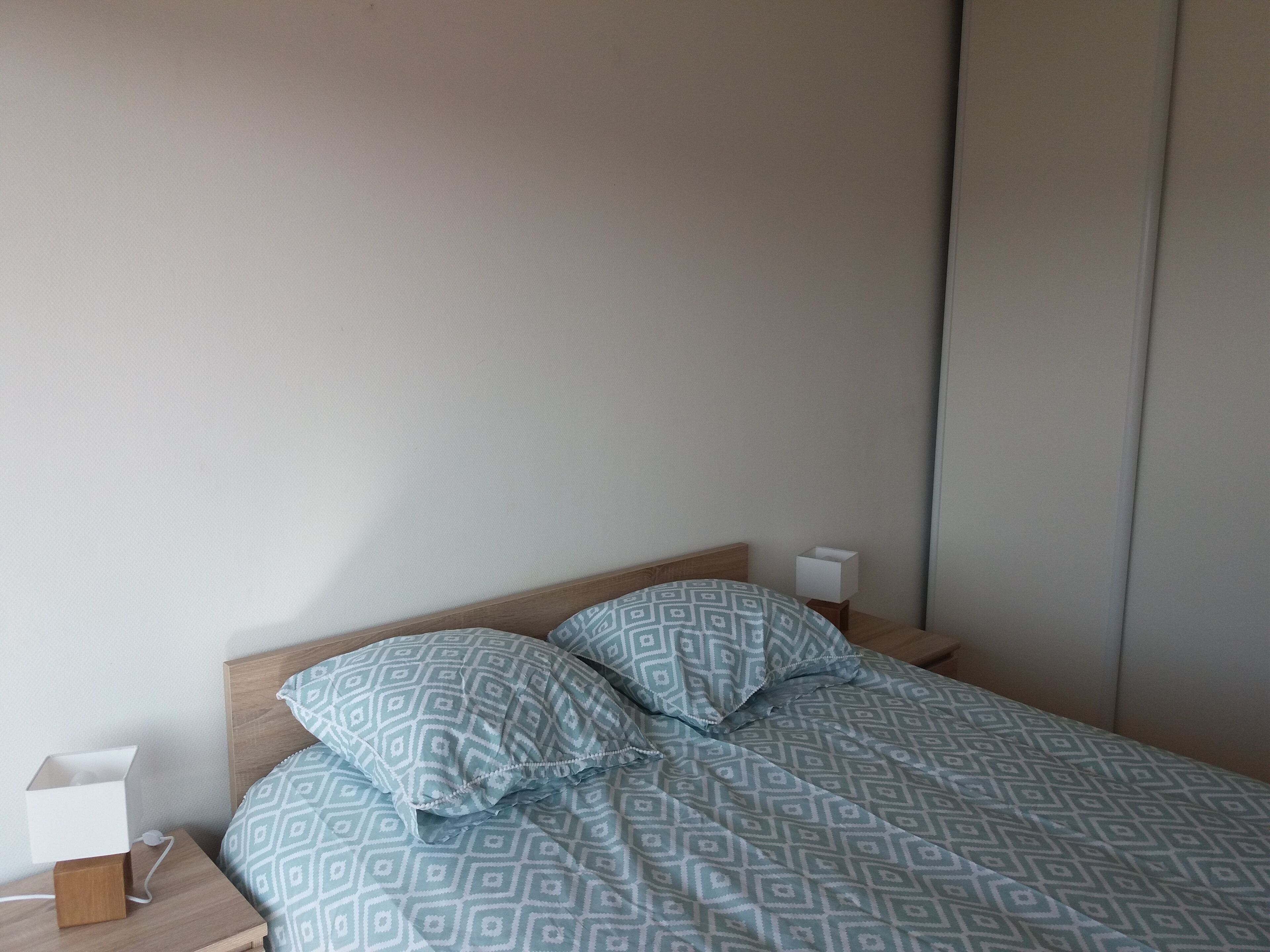 Ein ordentlich bezogenes Bett mit gemusterten Bettwäsche, ein Holz-Kopfteil und ein Nachttisch mit Lampe und einer Schachtel.