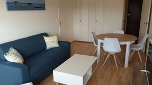 Een kamer met een blauwe bank, een witte salontafel, een eettafel met stoelen en een kledingkast.
