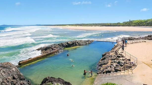 Zona de baño costera con agua cristalina, bordes rocosos y una playa arenosa.