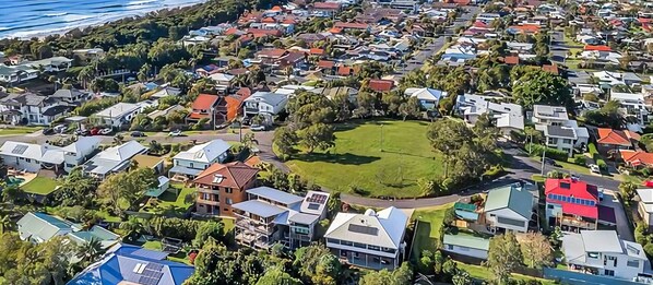 An aerial view of a residential area with houses, a central green space, and a body of water in the background.