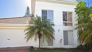 Una casa de dos pisos con garaje, una palmera y un pequeño jardín.