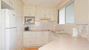 Una cocina compacta con armarios blancos, microondas, hervidor y pileta.