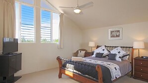Un dormitorio con cama, mesitas de noche, televisor y ventilador de techo.