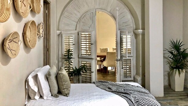 A bedroom with a bed, pillows, a plant, and a doorway leading to another room.