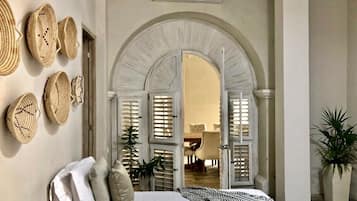 A bedroom with a bed, pillows, a plant, and a doorway leading to another room.