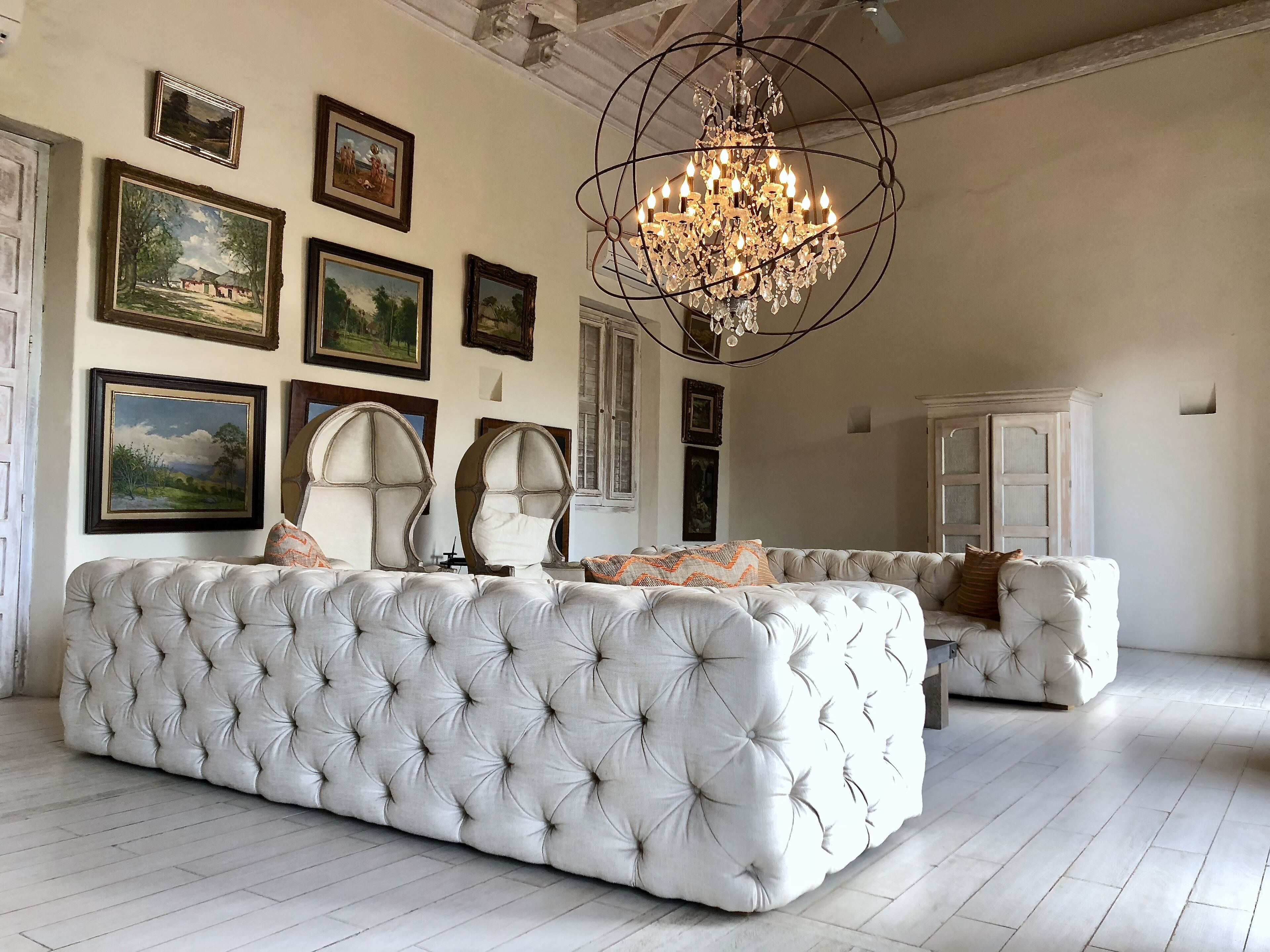 A spacious living room with a large, tufted sofa set, a chandelier, and several framed artworks on the walls.