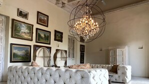 A spacious living room with a large, tufted sofa set, a chandelier, and several framed artworks on the walls.