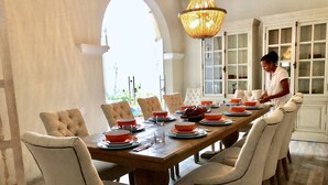 A dining room with a long wooden table set for a meal, surrounded by upholstered chairs.