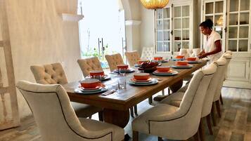 A dining room with a long wooden table set for a meal, surrounded by upholstered chairs.