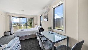 Ein Hotelzimmer mit einem Bett, einem Schreibtisch und Stühlen. Große Fenster bieten einen Blick ins Freie.
