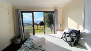 Habitación de hotel con una cama grande, vistas al exterior y una mesita con una lámpara.
