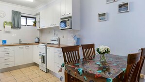 A modern kitchen with white cabinets, a microwave, a stove, and a dining table with chairs. - Ocean Sands 5 is a fully furnished two bedroom unit located on the first floor, next to the beach. (Sawtell)