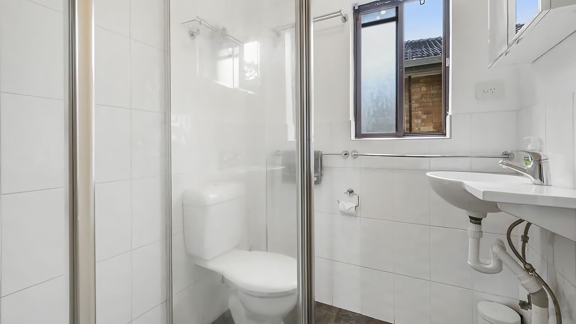 A modern bathroom with a glass shower enclosure, a white toilet, and a sink with a mirror above it.