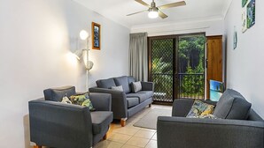 A living room with a sofa set, a floor lamp, and a ceiling fan. - Ocean Sands 5 is a fully furnished two bedroom unit located on the first floor, next to the beach. (Sawtell)