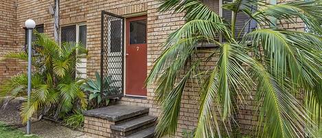 A brick building with a red door, a small front porch, and a number '7' on the door.