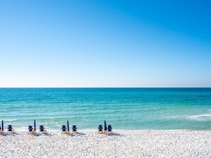 Une plage de sable blanc, sous un ciel bleu azur. Plusieurs chaises longues sont alignées en rangée le long du rivage.