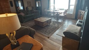 Un vaste salon doté d’un haut plafond, de poutres apparentes, d’une cheminée, d’un coin repas avec des chaises et d’un téléviseur.