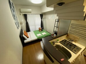 Een compacte kamer met een bed, een kitchenette en een raam met gordijnen.