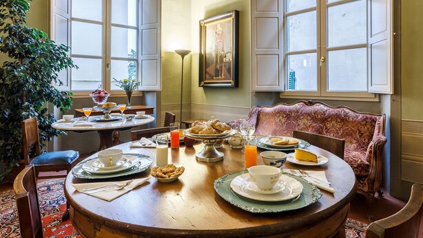 Un comedor con una mesa redonda dispuesta para el desayuno, con platos, tazas y diversos alimentos.