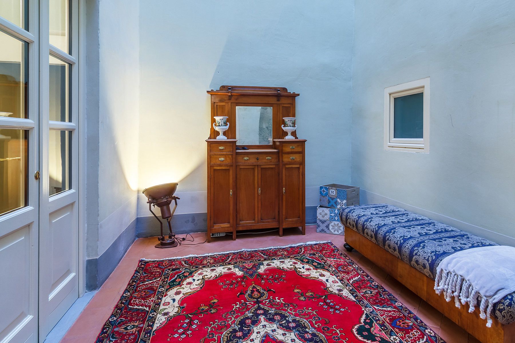 A room with a wooden wardrobe, a bed with a patterned bedspread, and a red carpet.